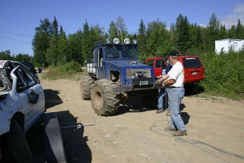 2003 Jeep TJ - Custom blue off-road truck with large tires, red SUV, and damaged white car are parked outdoors.