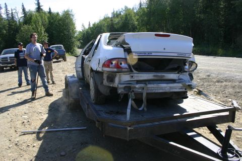2003 Jeep TJ - A damaged white Chrysler sedan is loaded onto a trailer, with several people observing the scene.
