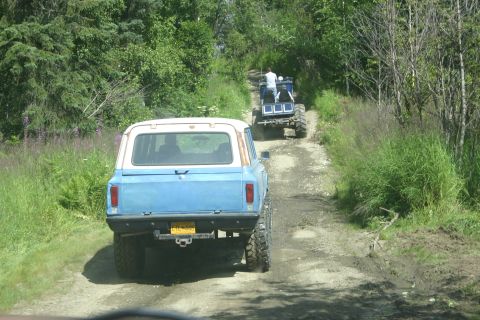 2003 Jeep TJ - Two off-road vehicles navigate a muddy dirt path surrounded by lush green foliage.