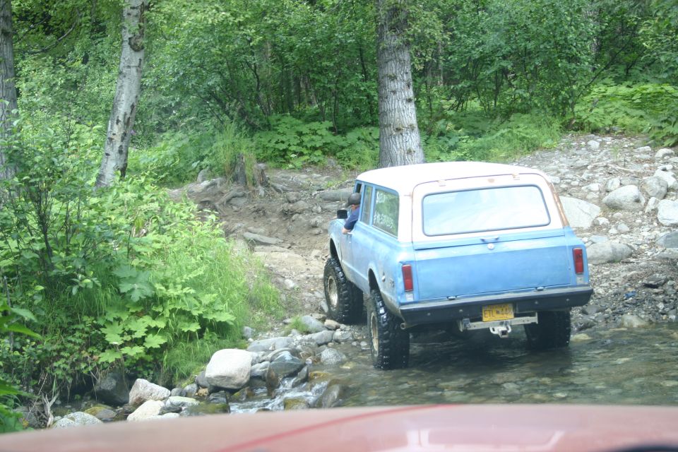 Blue and white SUV with lifted suspension driving through a shallow stream on a rocky trail