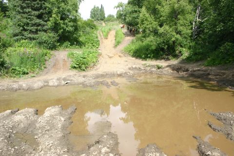 2003 Jeep TJ - Off-road trail with a large muddy puddle and a steep dirt path ahead.