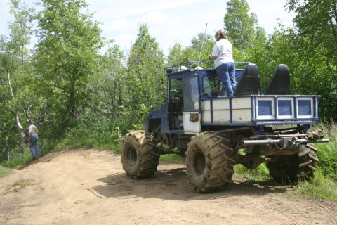 2003 Jeep TJ - A custom-built off-road vehicle with oversized tires is parked on a dirt path surrounded by trees.