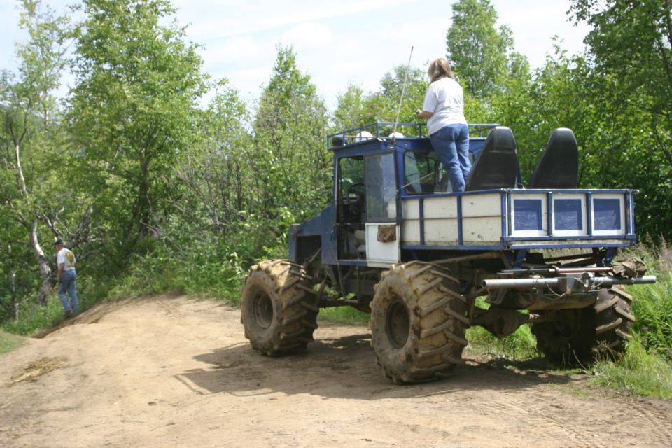 Blue custom off-road vehicle with large tires, a flatbed, and a cab, seen from the rear