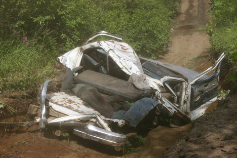 2003 Jeep TJ - A severely damaged vehicle lies off a dirt path, its interior and mangled bodywork visible.