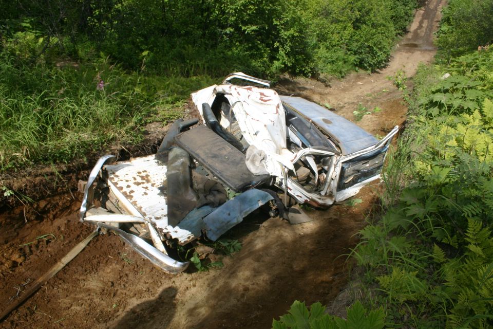 Wrecked white and blue car on dirt road, 3q-front view