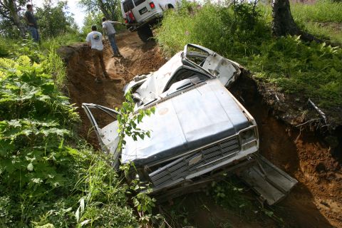 2003 Jeep TJ - A pickup truck has gone off-road and is stuck in a ditch, with a white van nearby.
