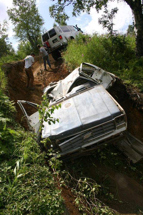2003 Jeep TJ - Two vans are stuck on a steep, muddy incline with one vehicle heavily damaged in the foreground.