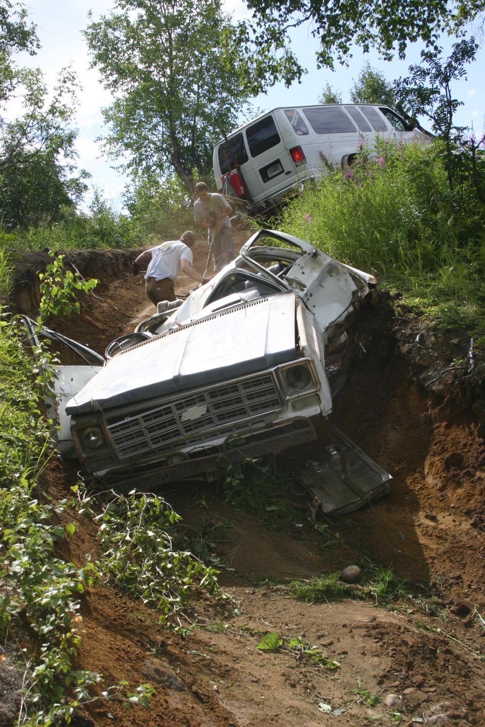 White pickup truck and van stuck on a dirt hill with people trying to help