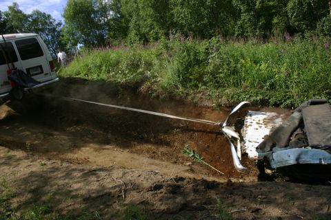 2003 Jeep TJ - A white van tows a blue vehicle out of a muddy ditch, surrounded by green foliage and trees.