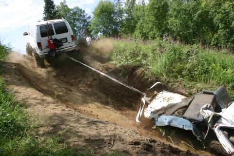 2003 Jeep TJ - A white van is used to tow a wrecked vehicle up a steep, dusty dirt incline, with two people visible in the background.
