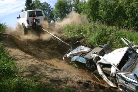 2003 Jeep TJ - A van tows a wrecked car up a steep, dusty incline in a wooded area.
