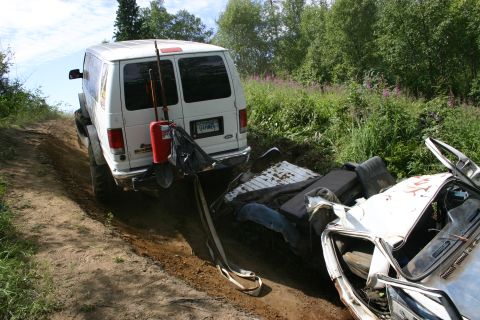 2003 Jeep TJ - A white van is parked on a dirt path next to debris from a wrecked vehicle.