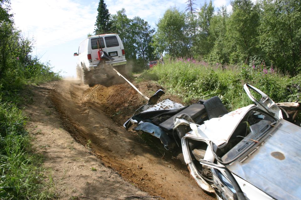 White van towing wrecked car up a dirt hill