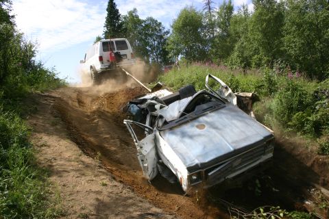 2003 Jeep TJ - Van tows wrecked car up a steep, dusty dirt path surrounded by vegetation.