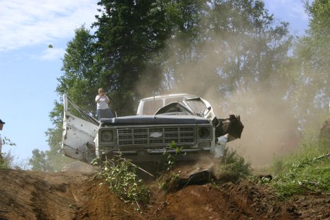 2003 Jeep TJ - A severely damaged pickup truck is stuck on a dirt hill, kicking up dust as onlookers watch.
