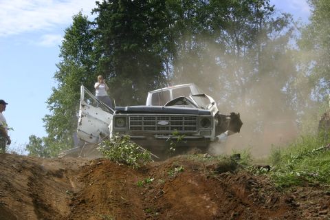2003 Jeep TJ - A heavily damaged 1973 Chevrolet C/K truck is seen on a dirt track, with dust in the air and trees in the background.