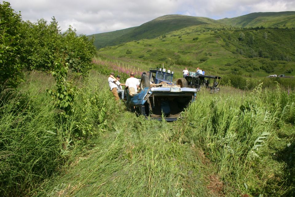 Blue Jeep TJ overturned in tall grass with people around it