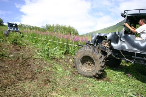 2003 Jeep TJ - Two off-road vehicles are engaged in a tug-of-war on a steep, grassy incline with scattered wildflowers.
