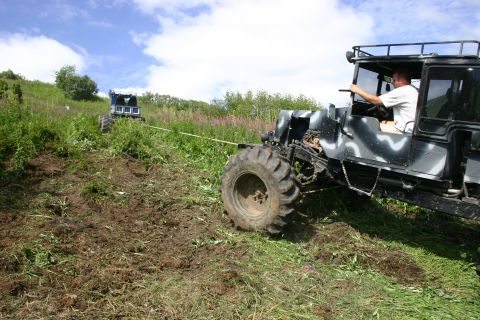 2003 Jeep TJ - Two off-road vehicles are engaged in a tow operation on a steep, grassy incline under a partly cloudy sky.