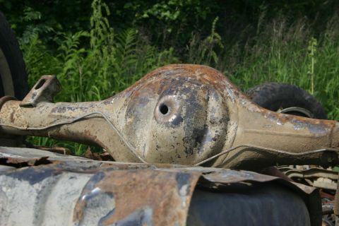 2003 Jeep TJ - A close-up view of a heavily rusted differential housing, likely from an older vehicle, set against a backdrop of green foliage.