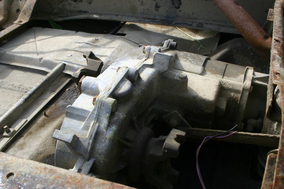Transfer case assembly with visible bolts and wiring. Some rust on surrounding frame parts