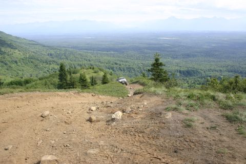 2003 Jeep TJ - A vehicle navigates a challenging off-road path with a scenic vista of forests and mountains.