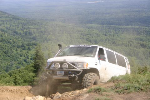 2003 Jeep TJ - Modified van tackling an off-road trail with a scenic forest backdrop.