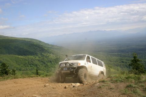 2003 Jeep TJ - A modified white van navigates a dusty, off-road trail with a scenic mountain vista in the background.