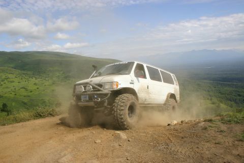2003 Jeep TJ - A white van navigates a dusty trail on a grassy hillside with mountains in the distance.