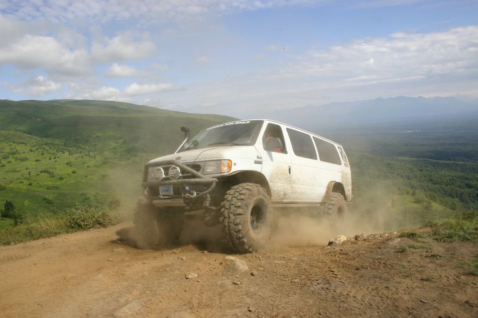 White van with off-road tires and bumper driving on a dirt path, kicking up dust