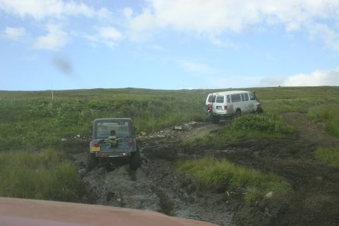 2003 Jeep TJ - Two off-road vehicles navigate a challenging muddy track on a grassy hillside.