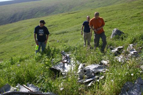 2003 Jeep TJ - Wreckage is visible in a grassy field with three individuals observing the scene.