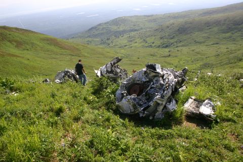 2003 Jeep TJ - Debris from a crashed aircraft lies strewn across a green, rolling hillside under a hazy sky.