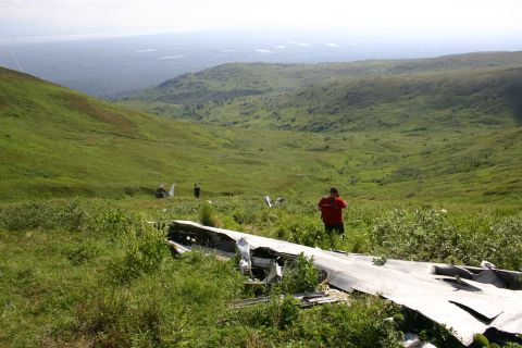 2003 Jeep TJ - Airplane wreckage is visible in a vast, green, hilly landscape with two people observing.