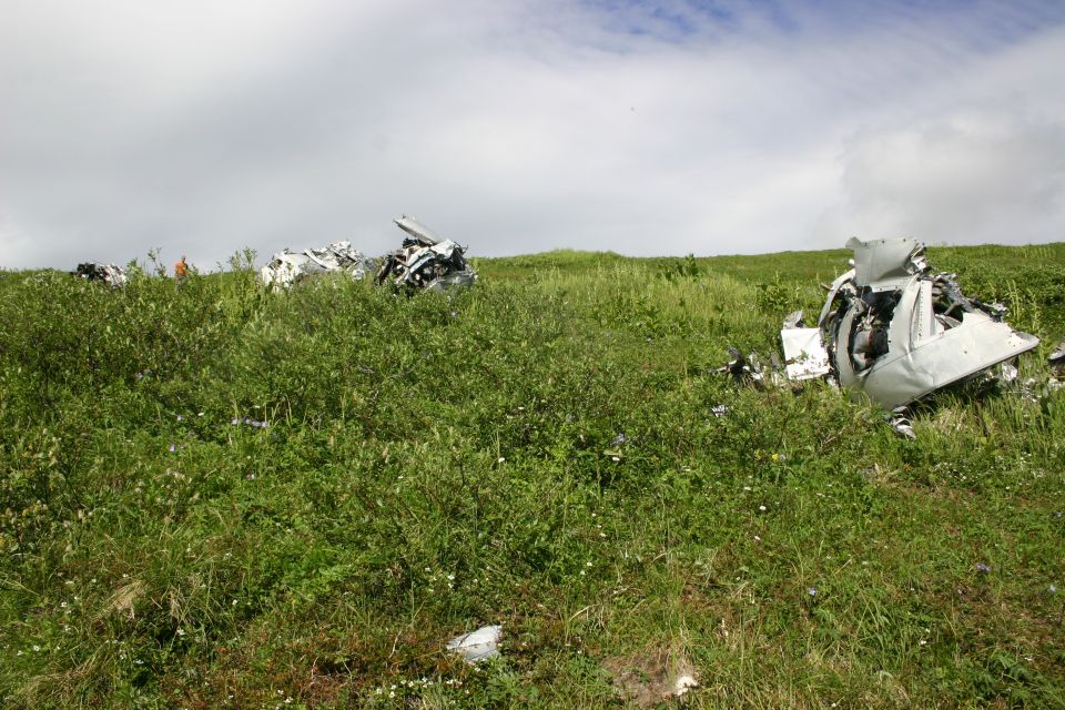 Debris scattered across a grassy slope under a cloudy sky