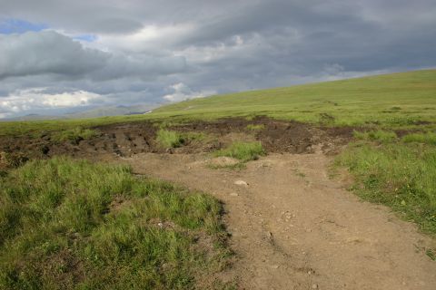 2003 Jeep TJ - A dirt road leads through a grassy landscape with disturbed earth on the hillside.