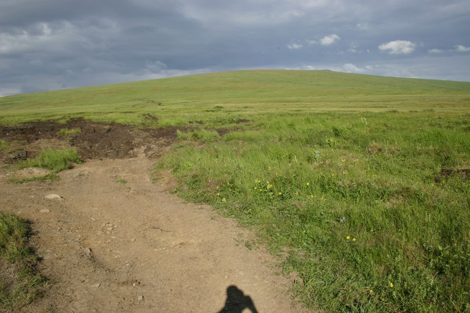 Dirt path leading to a grassy hill under a cloudy sky