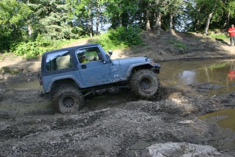2003 Jeep TJ - A blue Jeep Wrangler tackles a challenging muddy obstacle course, demonstrating its off-road capabilities.