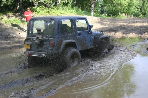 2003 Jeep TJ - A Jeep TJ navigates a muddy obstacle course, kicking up a significant amount of water and mud.