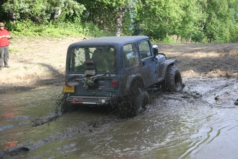 2003 Jeep TJ - A dark blue Jeep Wrangler navigates a muddy trail, kicking up water and dirt.