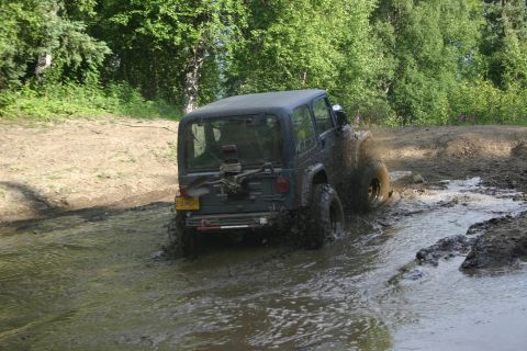 2003 Jeep TJ - A dark Jeep Wrangler navigates a muddy trail, kicking up water and mud as it drives through a shallow water crossing.