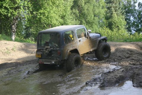 2003 Jeep TJ - Jeep TJ tackling off-road terrain, covered in mud after driving through a water obstacle.
