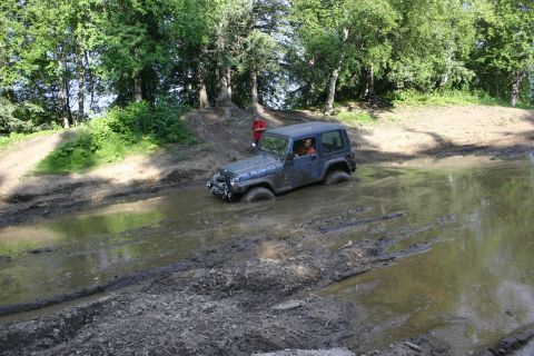 2003 Jeep TJ - A Jeep Wrangler navigates through a muddy off-road trail, getting stuck in a deep puddle.