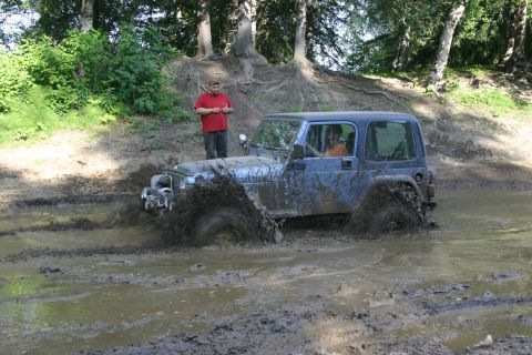 2003 Jeep TJ - A blue Jeep Wrangler navigates a muddy terrain, kicking up a significant amount of water and mud.