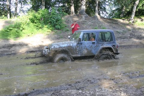 2003 Jeep TJ - A blue Jeep TJ navigates a muddy trail, kicking up water and dirt.