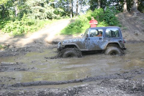 2003 Jeep TJ - A Jeep Wrangler TJ navigates a challenging muddy terrain, with one wheel deep in the mire.