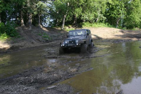 2003 Jeep TJ - This Jeep TJ is navigating a muddy off-road course with trees in the background.