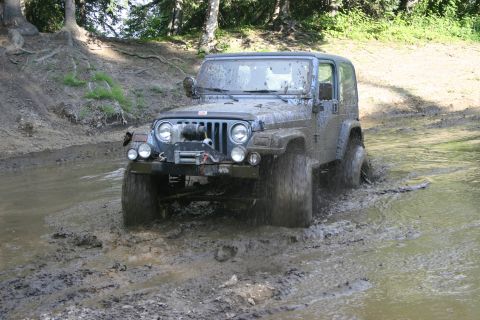 2003 Jeep TJ - A blue Jeep Wrangler navigates a muddy trail, kicking up water and dirt.