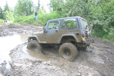 2003 Jeep TJ - A Jeep TJ navigates a challenging muddy terrain, with a second vehicle in the distance.