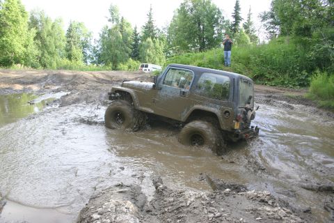 2003 Jeep TJ - A Jeep TJ navigates a challenging muddy terrain, with another vehicle visible in the distance.